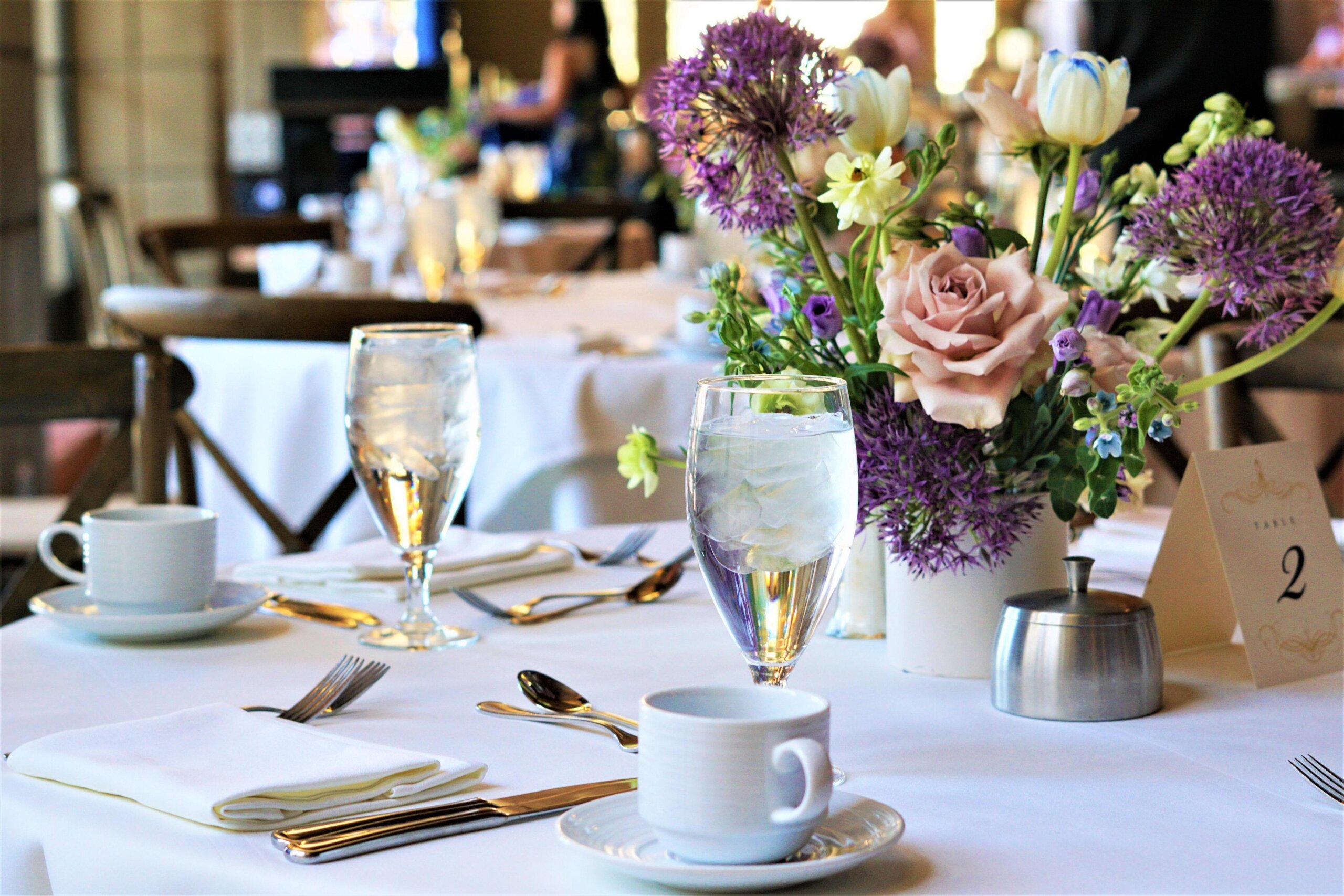 Cover Image for Dining room at The Gold Room. The tables are covered in a white tablecloth and have flowers on them.