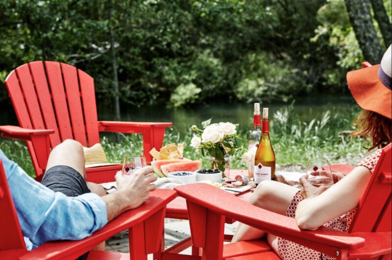 Two people sitting in red lawn chairs with glasses of wine
