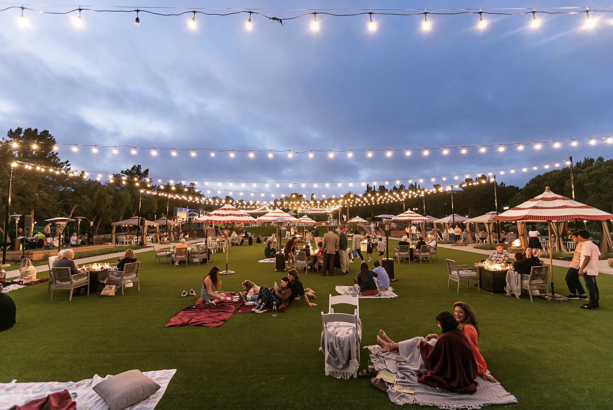 Cover Image for Open lawn area with string lights and people sitting on blankets and benches at the Fairmont Grand Del Mar