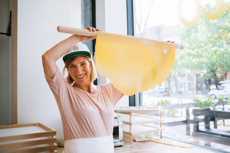 Person holding up a hand-rolled sheet of pasta in front of a window