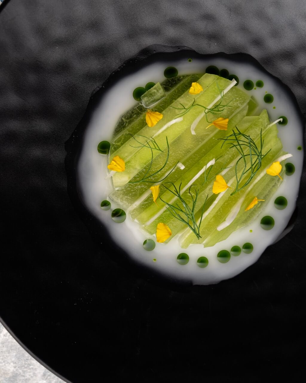 Vibrant green and white dish with dill and yellow edible flower petals on large black plate