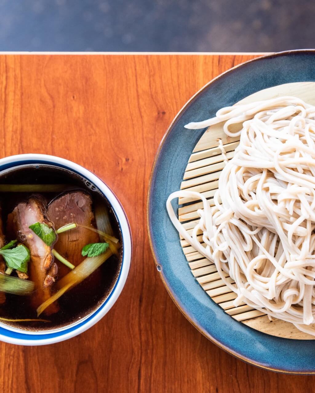 Small bowl of broth and meat next to large plate of soba noodles