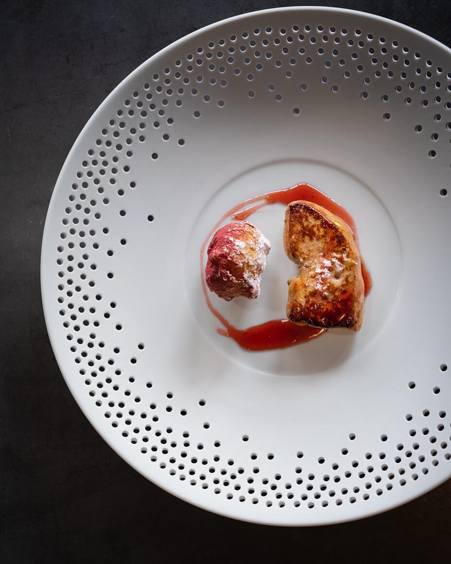 Seared foie gras dish on large white plate with pattern of holes