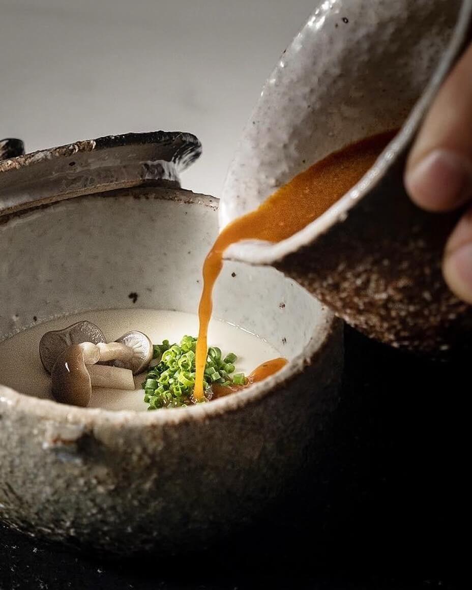 Broth being poured into bowl with mushrooms and chives