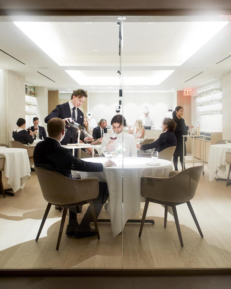 Server pouring wine into a carafe at a table with two guests at Atera’s
