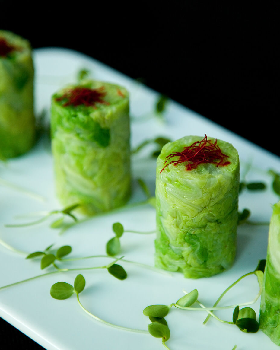 Four green cylindrical canapé lined up on a rectangular white plate