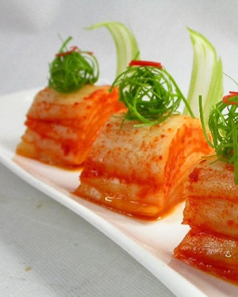 Three canapé lined up on a rectangular white plate that resemble kimchi
