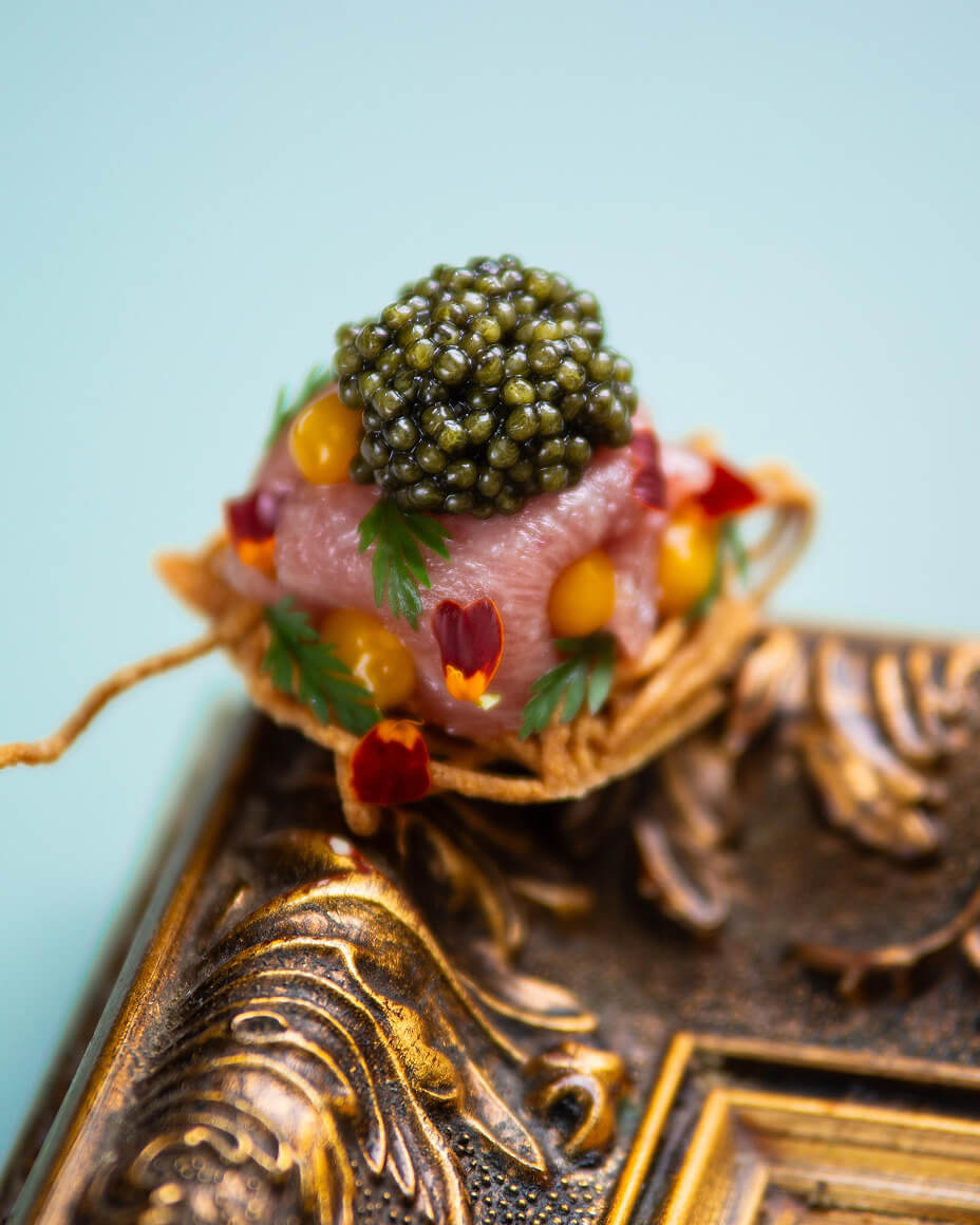 Small canapé topped with caviar and edible flowers on top of the corner of a picture frame