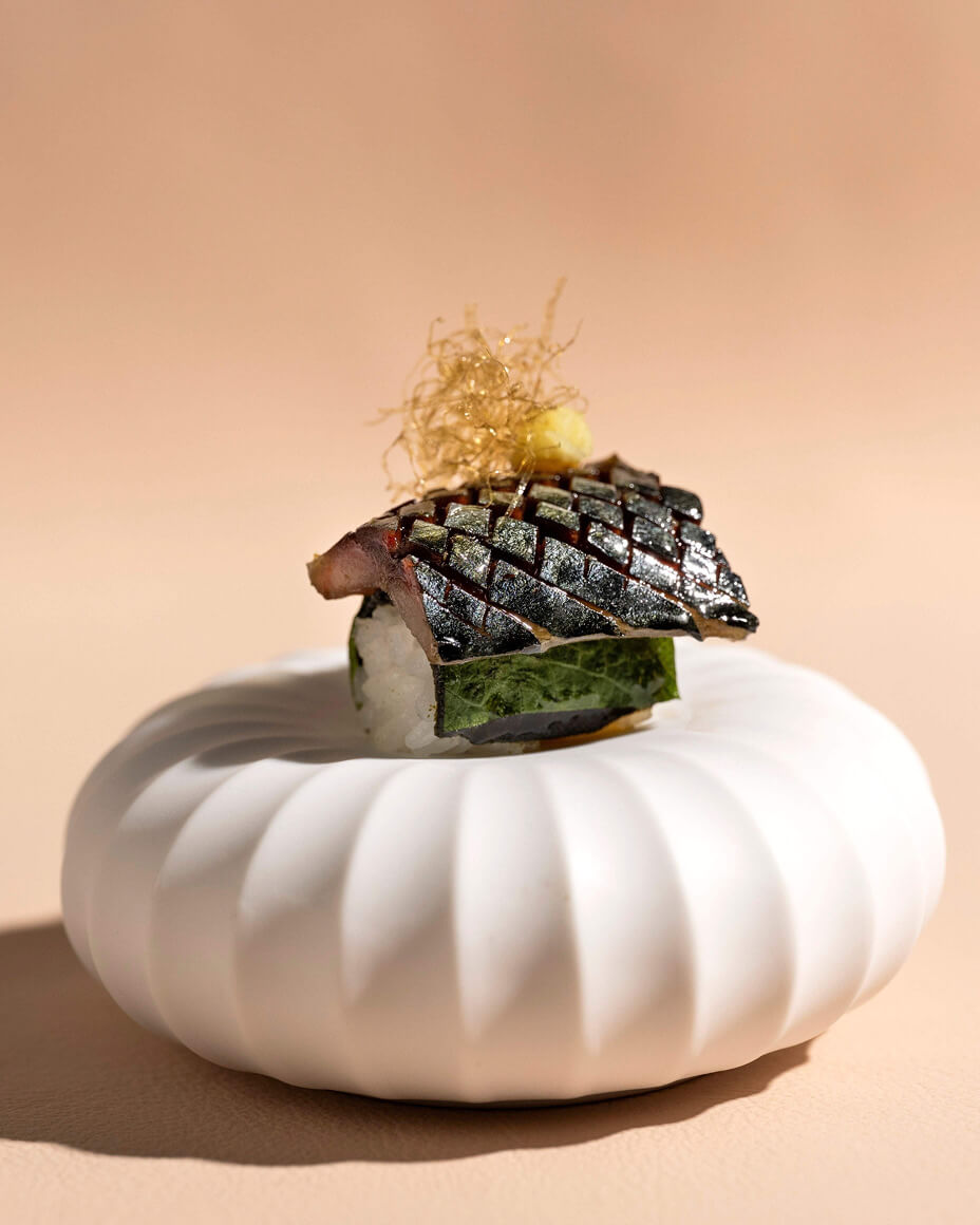 Small bite resembling nigiri placed on top of pillow-like white ceramic plate