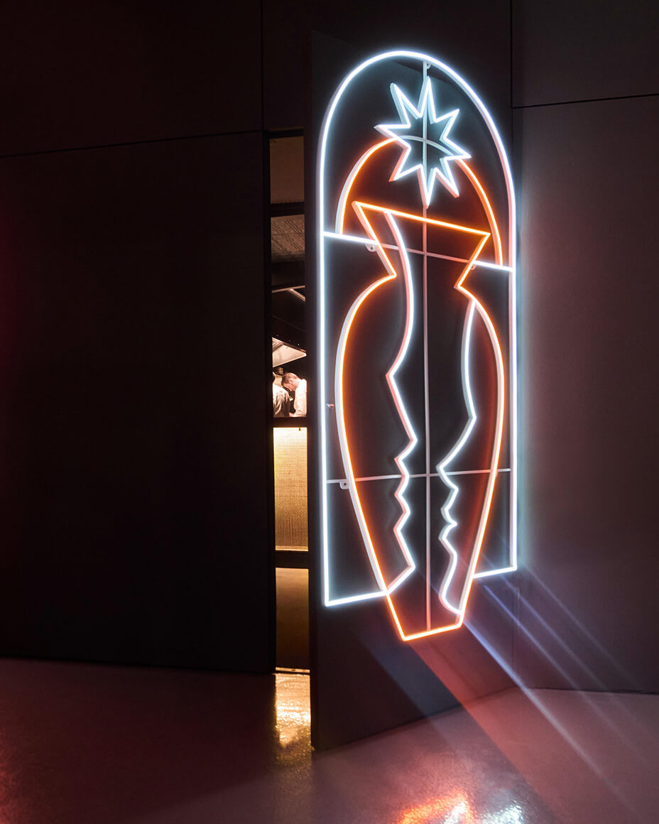 Neon art piece attached to a door that is slightly ajar unveiling a peek into FREVO’s kitchen and counter