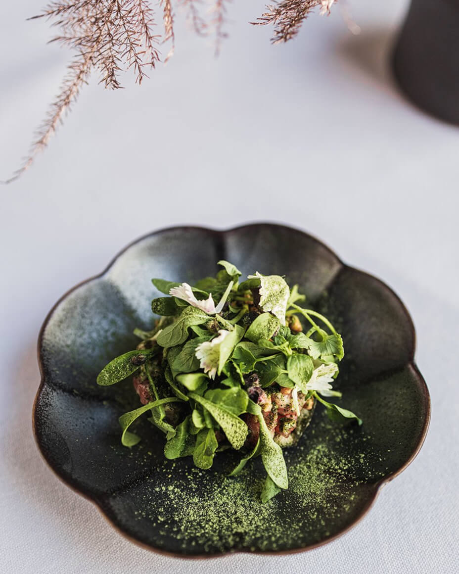 Wagyu tartare with microgreens on a black flower-like plate on a white tablecloth
