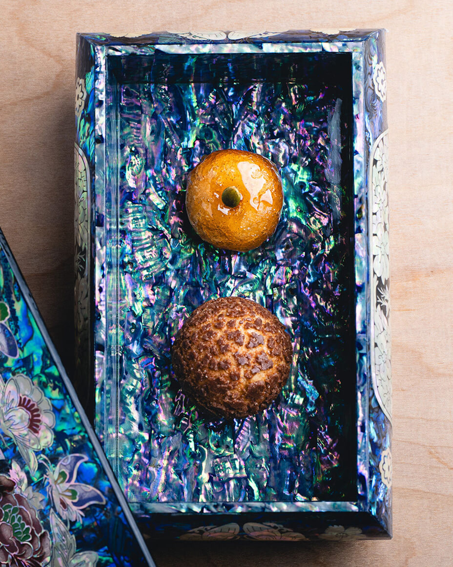 Ornate pearlescent purple and green box with two round brown-orange bites of food