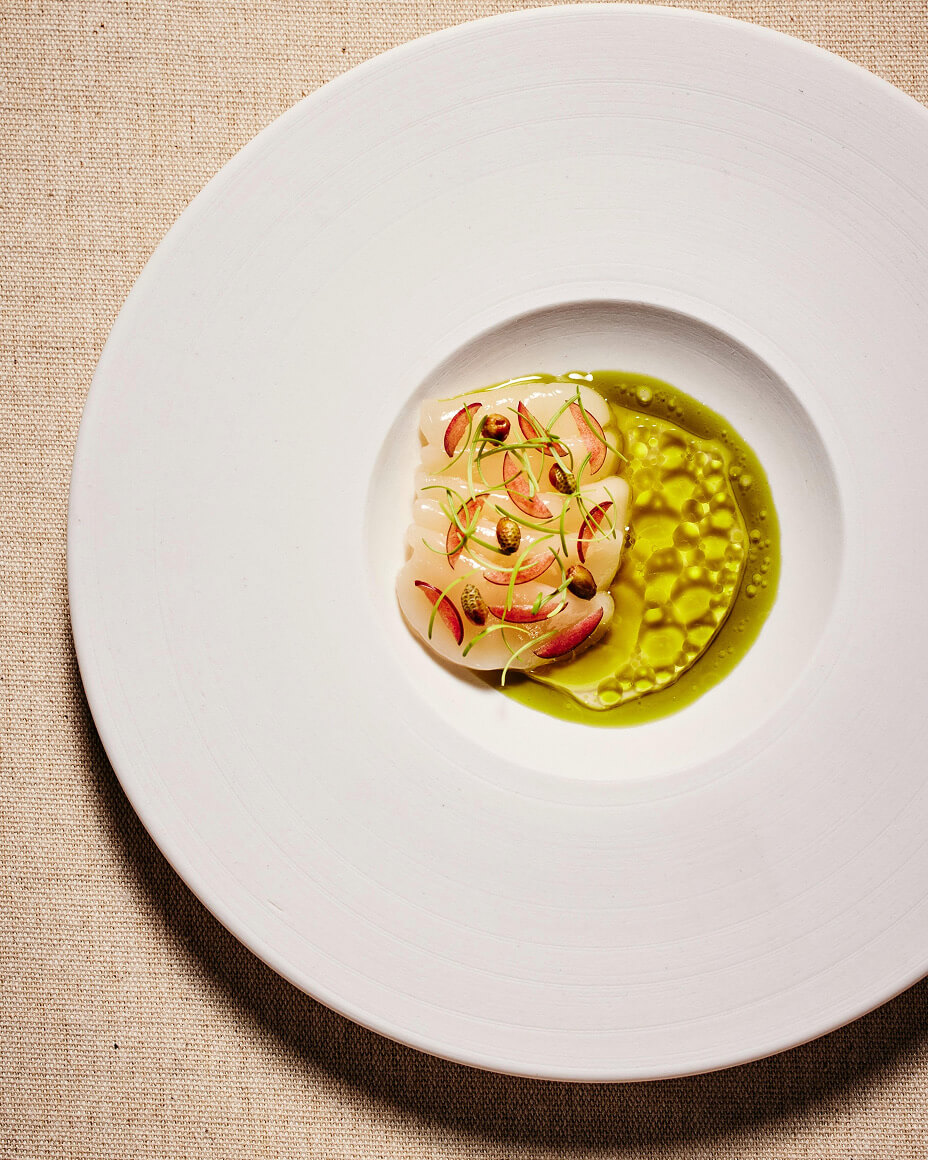 Large wide-rim bowl with plated slices of raw fish in a separated oil and vinegar sauce