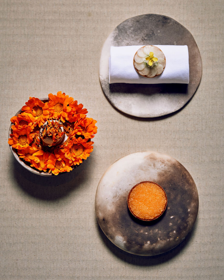 Three hand-thrown plates, two with bright orange bites and one with a white and yellow food arrangement