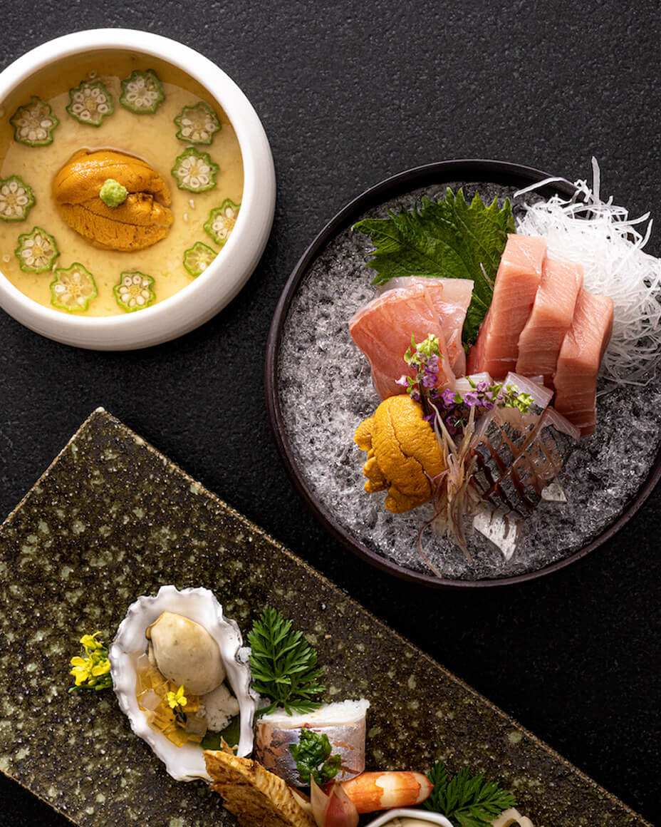 Overhead of three plated dishes, one with uni and okra, slices, one with sashimi, and one with an oyster