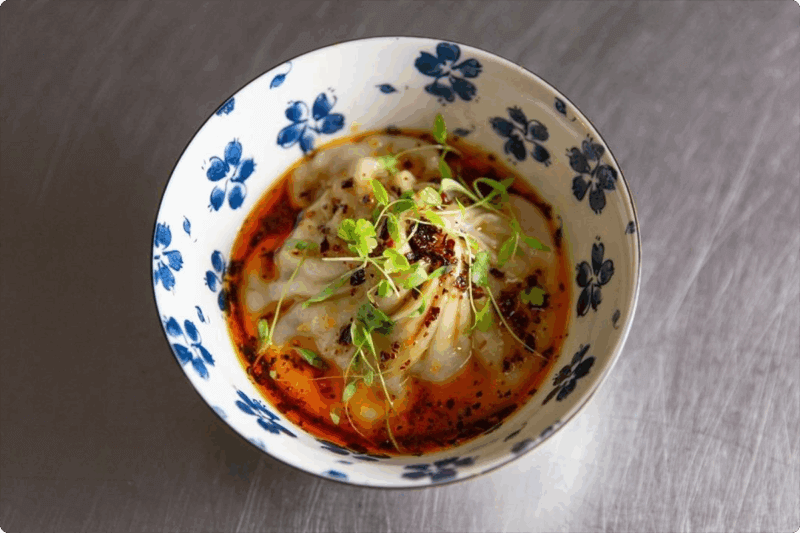 Large dumpling in a white and blue patterned bowl with chili oil and microgreens